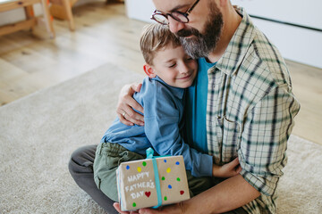 Dad get a handmade gift from little son, present wrapped in diy homemade wrapping paper. Father embracing boy. Happy Fathers day concept.