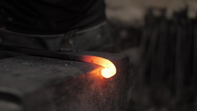 Closeup footage of a blacksmith manually forges molten metal on anvil in smithy with a hammer