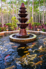 Water dripping from the fountain into the pond filled with koi fishes - obrazy, fototapety, plakaty