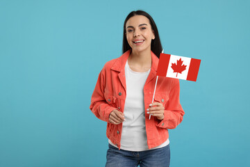 Happy young woman with flag of Canada on light blue background