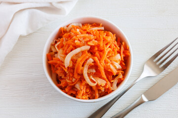 Fresh healthy vegetarian carrot salad with apple, onion and spices in the bowl with fork and knife. Top view, close up
