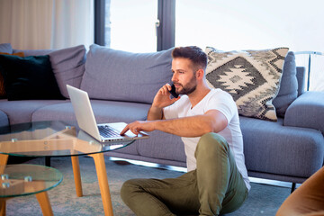 Confident man using laptop and smartphone at home for work - 785043077