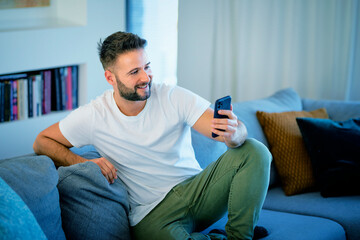  Handsome man relaxing on the sofa at home and using a smartphone