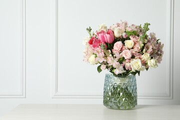 Beautiful bouquet of fresh flowers in vase on table near white wall. Space for text