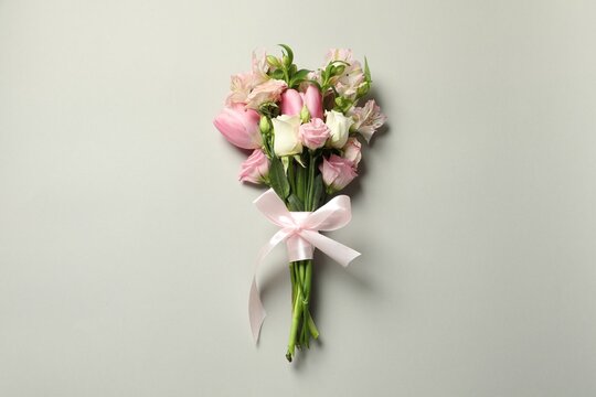 Happy Mother's Day. Bouquet of beautiful flowers tied with pink ribbon on light grey background, top view