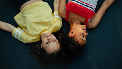 Teenager girls friends spending time outdoors in garden, laughing. Top view, lying on trampoline. Best friends forever.