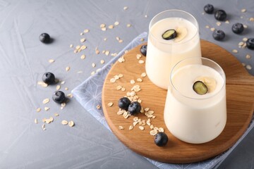 Tasty yogurt in glasses, oats and blueberries on grey table, space for text