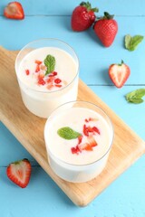 Tasty yogurt in glasses and strawberries on light blue wooden table