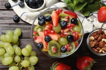 Tasty fruit salad in bowl and ingredients on wooden table, flat lay
