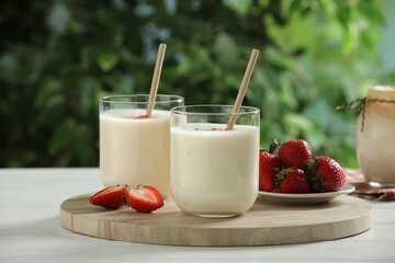 Tasty yogurt in glasses and strawberries on white wooden table outdoors