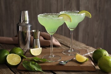 Delicious Margarita cocktail in glasses, limes and bartender equipment on wooden table