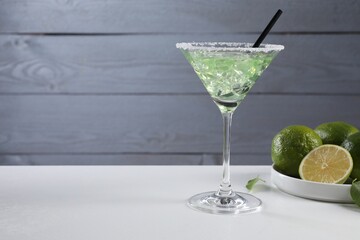Delicious Margarita cocktail with ice cubes in glass and lime on white table, space for text