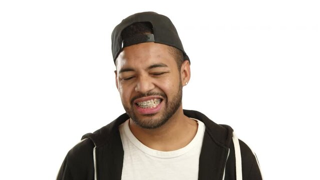 An Afro-American man with braces appears self-conscious and slightly embarrassed, his hand covering his mouth, hinting at a sense of shyness or a slip of the tongue on a white background. Camera RAW.