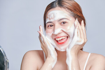 Smiling young woman washing foam face by natural foamy gel. satisfied girl with bare shoulders...