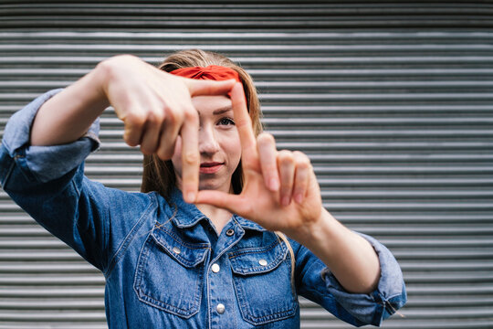 Young woman looking through finger frame in front of shutter