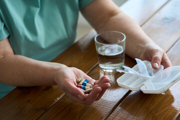 Woman holding capsules in hand by glass of water on table at home