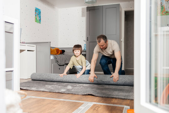 Boy helping father in unrolling carpet on floor at home