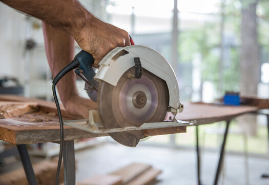 Carpenter cutting timber with electric circular saw at workshop