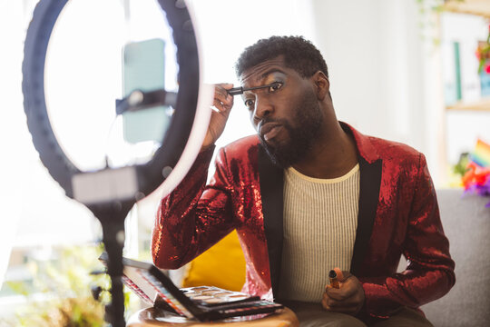 Non-binary person doing eye make-up near ring light at home