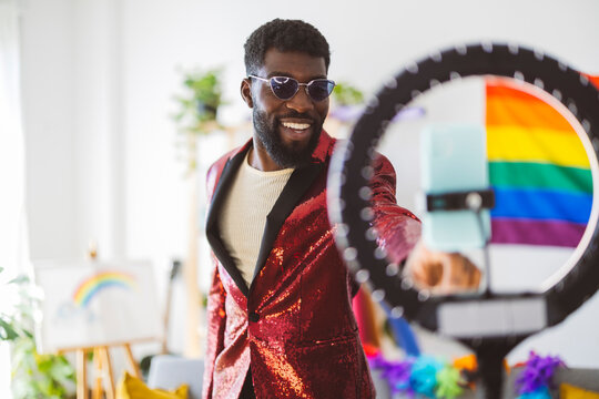Smiling non-binary person wearing sunglasses near ring light at home