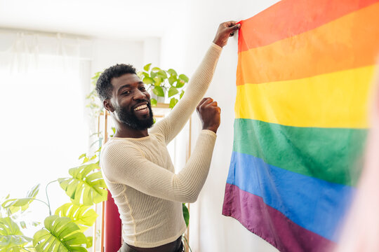 Happy non-binary person sticking rainbow flag on wall at home