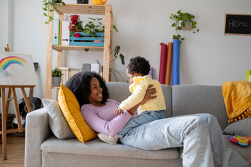 Smiling single mother lying on sofa playing with baby girl in living room at home