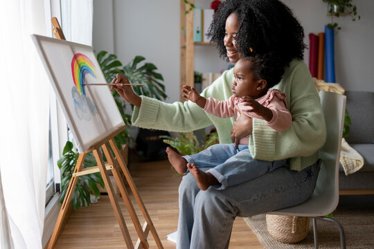 Smiling single mother painting rainbow with daughter at home