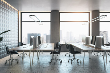 Modern office interior with desks, computers, and chairs on a concrete floor with a cityscape background. 3D Rendering