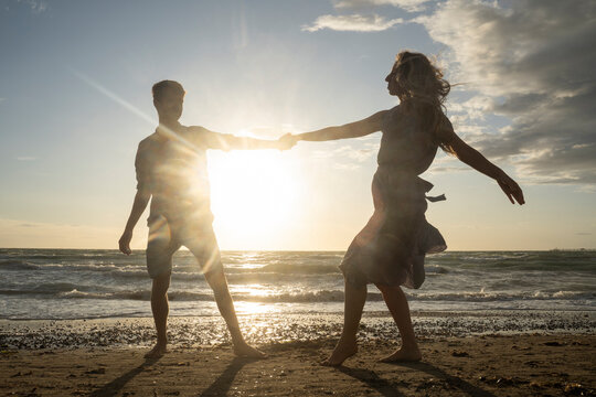 Back lit couple enjoying dance at windy beach