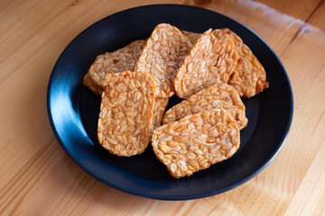 Tempeh, Tempe Goreng or Fried tempeh is Indonesian traditional food, made from fermented soybean seeds, served on a black plate