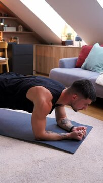 Man planking on yoga mat in living room, focusing on chest and arm strength