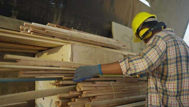 African American carpenter or woodworker or charpentier man use measuring tape to measure wood stick to prepare wood work in workplace.
