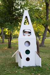 Child in astronauts wearing an astronaut helmet with toy cardboard rocket playing  in the park.  National Aerospace Week. Space Exploration Day. Moon Day. 
