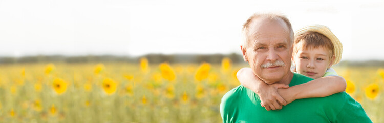  Concept of friendly family. banner. grandfather and grandson spend time together in nature. Copy space Little child boy hugs grandpa walking on the field with sunflowers on a summer day.  