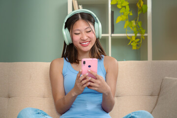 Beautiful woman with headphones listening to music on sofa happy shopping online with cell phone to...