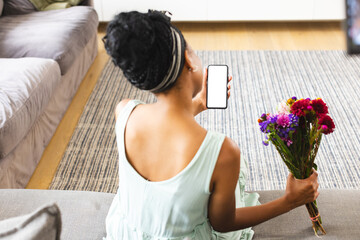 African American woman holding flowers, showing phone on a video call date with copy space