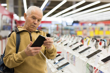 Elderly man examines tablet computer in showroom of electronics store
