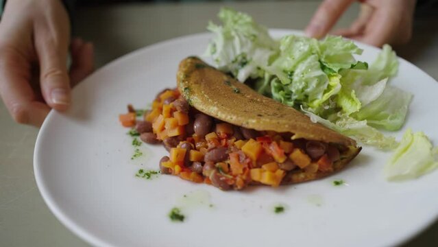 A healthy pita pocket filled with a mix of beans and diced vegetables is paired with a fresh green salad on a white plate, highlighting a nutritious meal. A healthy and delicious vegan dish.