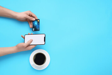 Online payment. Man with smartphone, credit card and coffee on light blue background, top view....