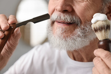 Man shaving mustache with blade in bathroom, closeup