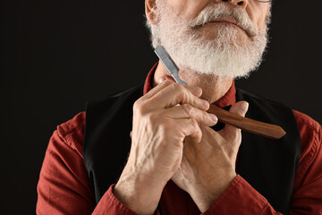 Man shaving beard with blade on black background, closeup