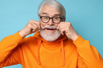 Senior man touching mustache on light blue background