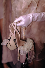 Woman's hand in a white glove holding elegant fashion high heel shoes with beads
