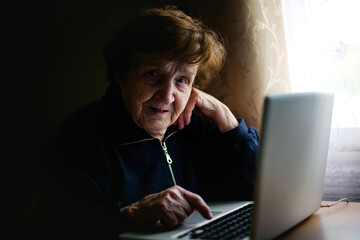 An aged woman engages with technology, her fingers tapping on a laptop keyboard. She bridges the gap between tradition and modernity, embracing the digital realm with wisdom. - 785096083