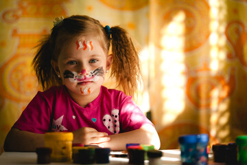 Portrait of a littie girl with her face adorned with bright paints, conveying a sense of creative...