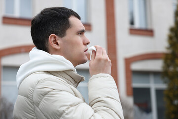 Sick young man with tissue on city street. Cold symptoms