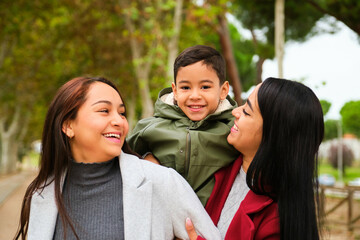 Portrait of happy Latin lesbian couple with their son in a park. LGBT family.