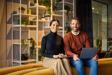 Portrait of a smiling man and woman, sitting on the couch, working over the laptop. - 785106297