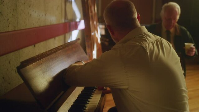 Sad man plays piano in front of an onlooker