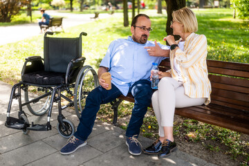Man in wheelchair is spending time with his mother in park. - 785111245